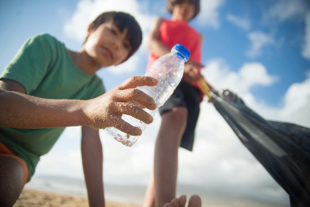 Children participating in a beach cleanup, collecting plastic bottles and trash on a sunny day.